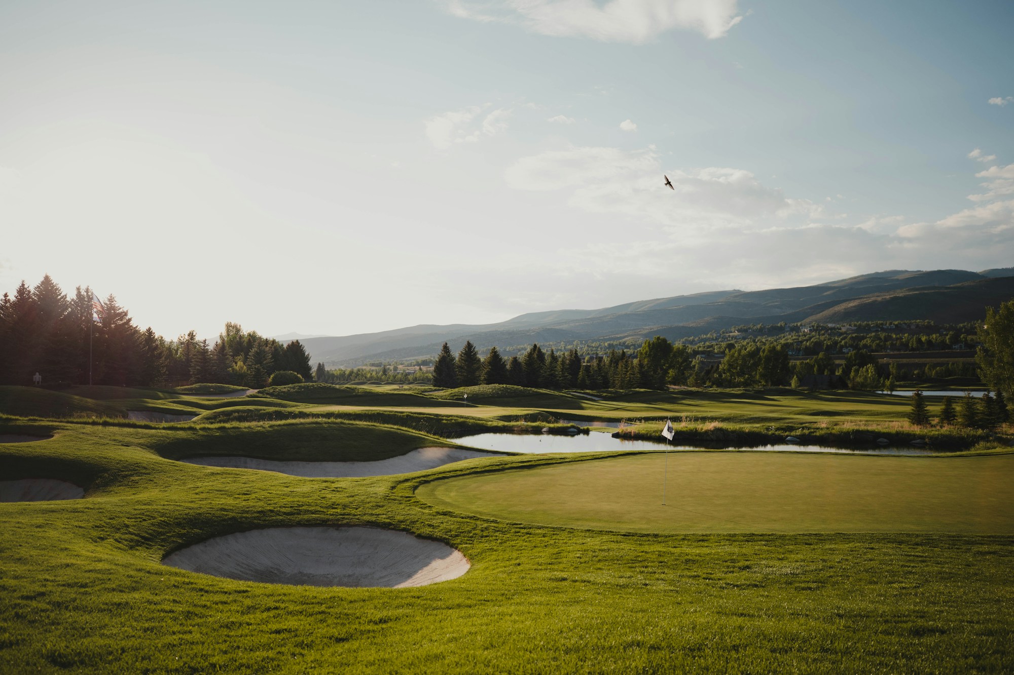 A green and bunkers under a soft white sky, mountains behind